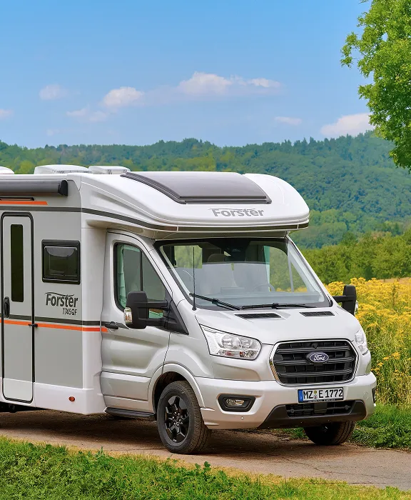 Ein teilintegriertes Forster Wohnmobil auf Ford-Basis steht auf einem Weg in einer grünen Hügellandschaft.