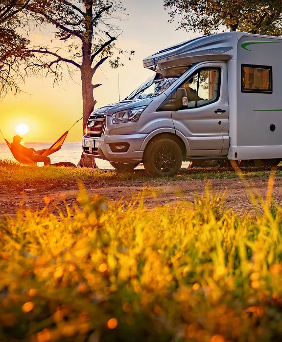 Forster Wohnmobil parkt am Wasser bei Sonnenuntergang; eine Person entspannt daneben in einer Hängematte.
